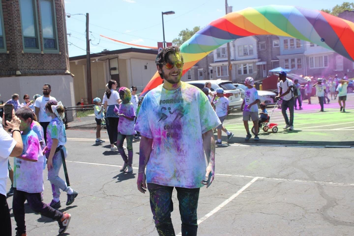 Joe Picozzi covered in colored powder at a neighborhood color run, surrounded by kids and families