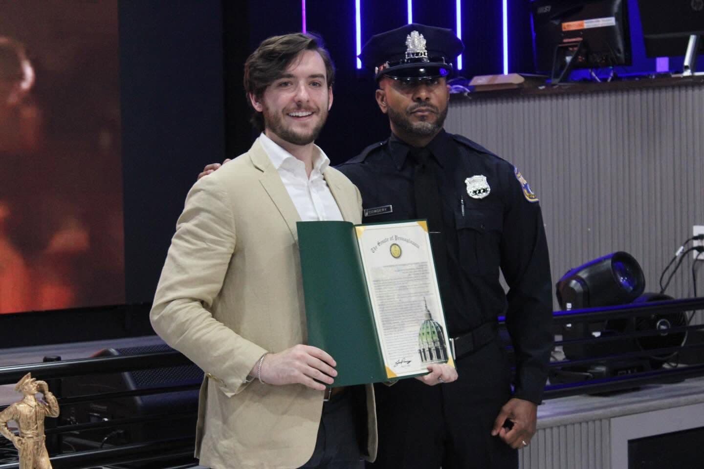 Joe Picozzi holding a Senate citation beside a Philadelphia police officer