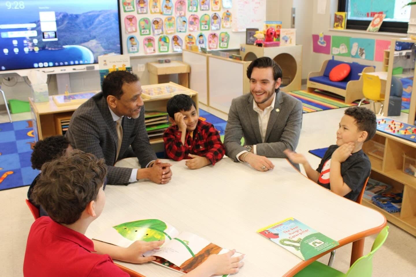 Joe Picozzi seated at a low table reading with preschool children