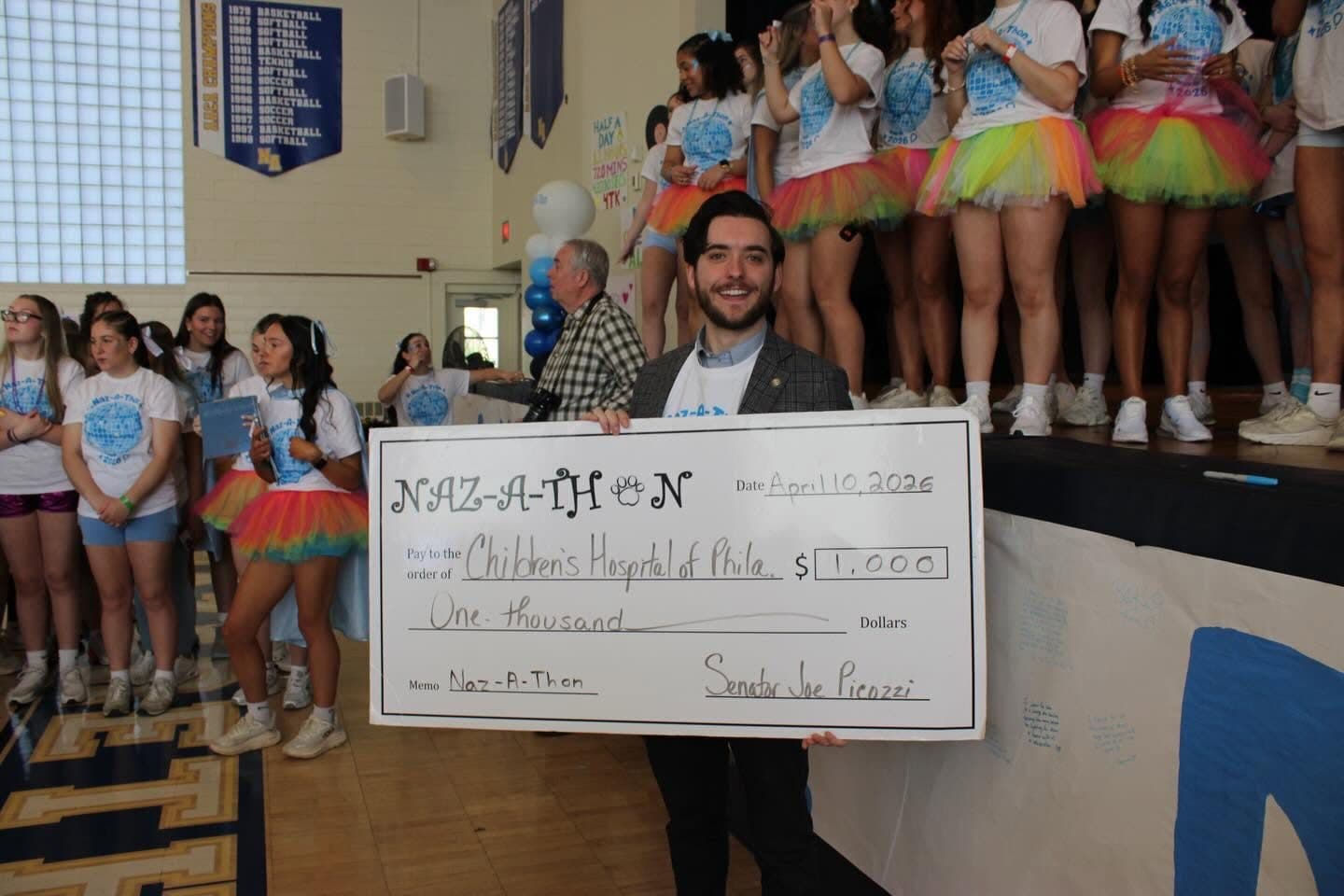 Joe Picozzi holding a giant check for Children's Hospital of Philadelphia in a gym full of Nazareth Academy students